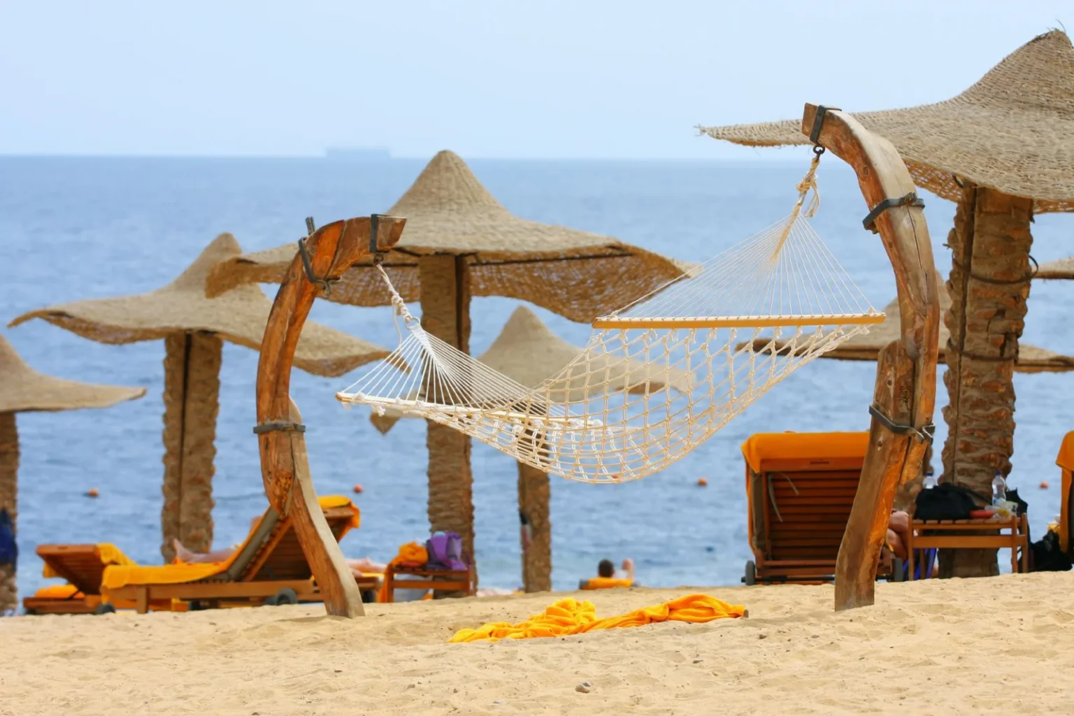 Tranquil beachside hammock under straw parasols with ocean view for perfect relaxation.