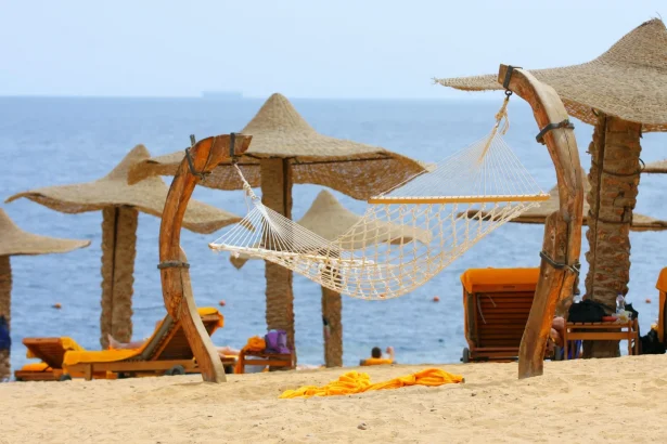 Tranquil beachside hammock under straw parasols with ocean view for perfect relaxation.