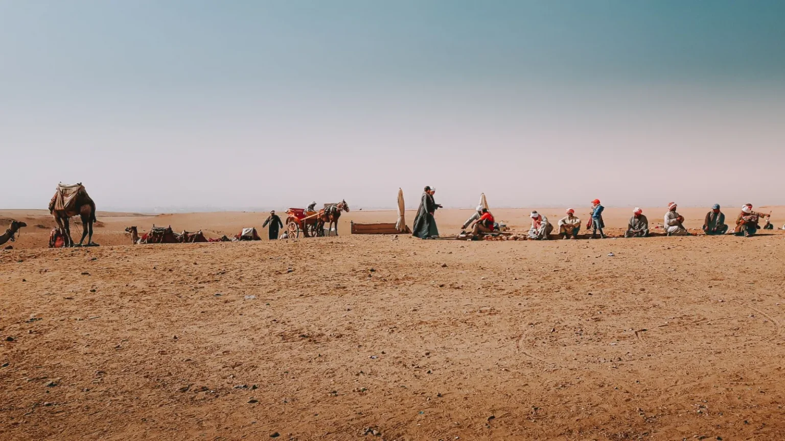 Bedouins with camels leading nomadic lifestyle resting in hot dry desert while traveling