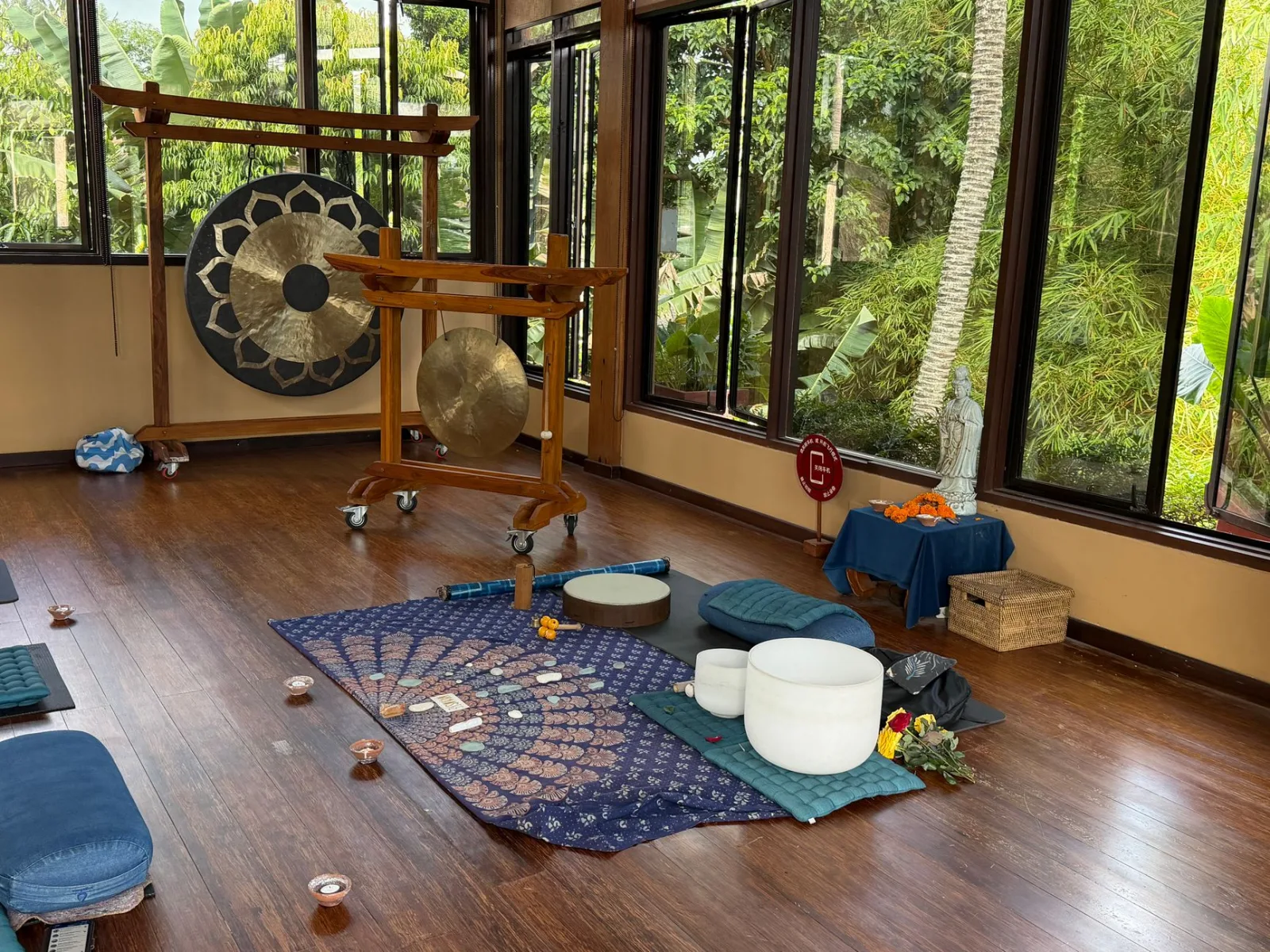 A serene meditation room with gongs, cushions, and mats, set in nature.