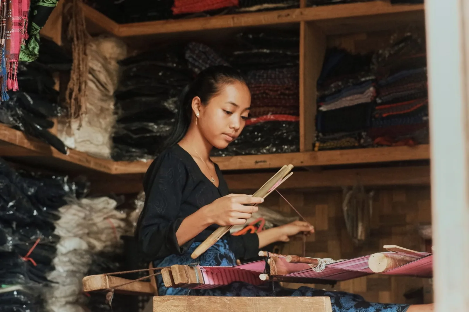 Young woman weaving traditional fabric, showcasing Banten's rich cultural heritage in a local shop setting.