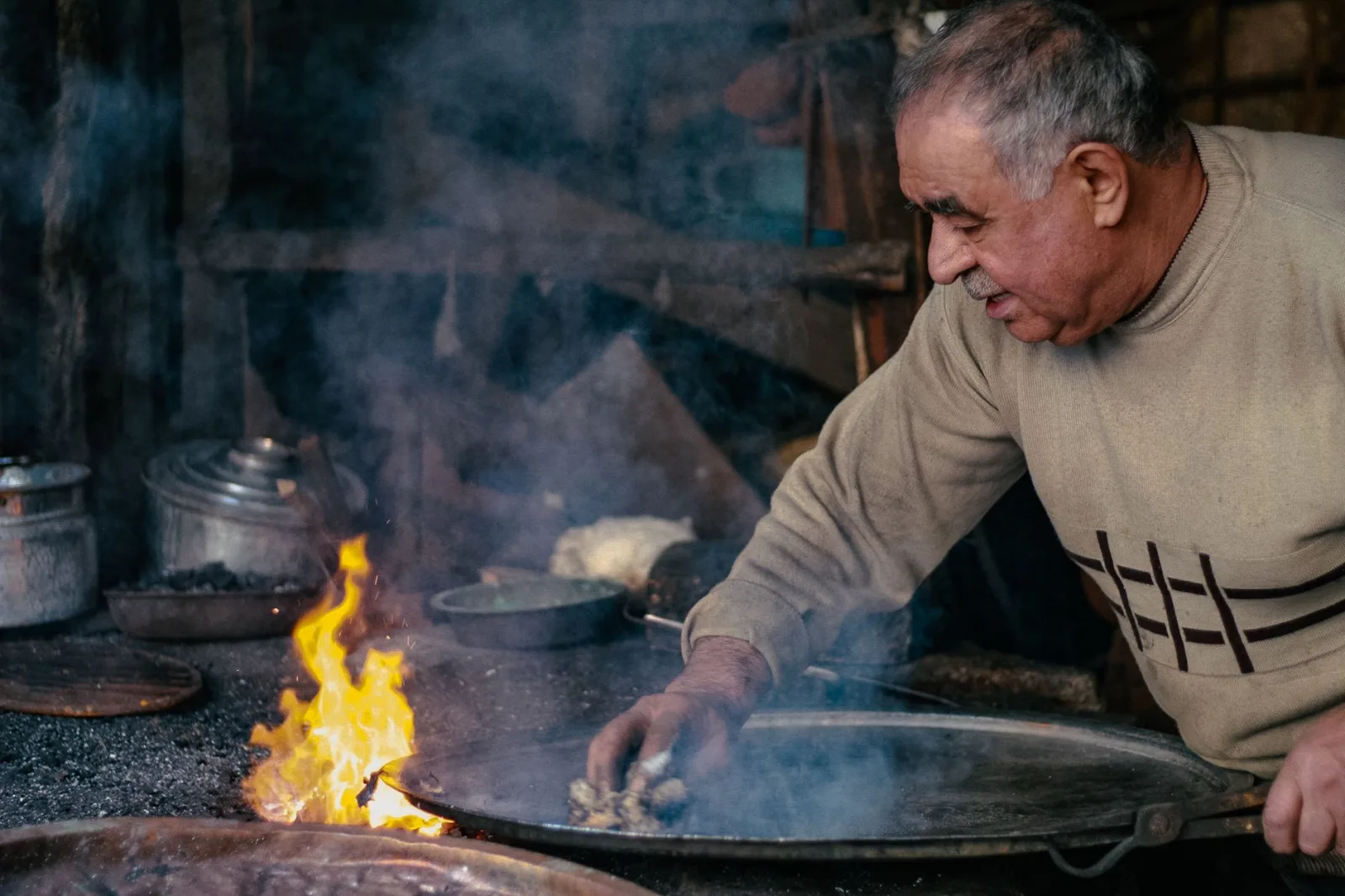 Senior man cooking with pots over an open flame in Denizli, Türkiye.