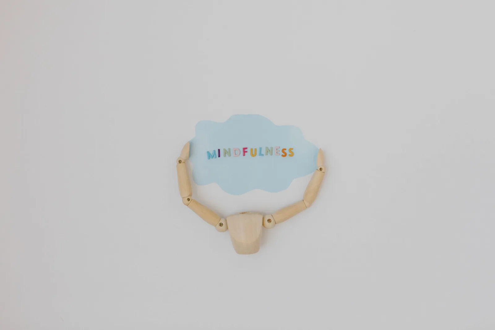 Minimalist image of a wooden figure holding a speech bubble saying 'Mindfulness'.