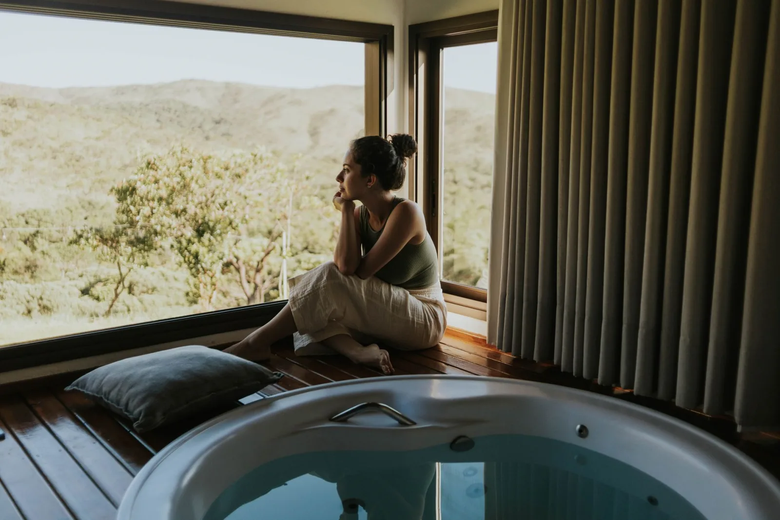 Woman gazing through window beside indoor jacuzzi overlooking mountains.
