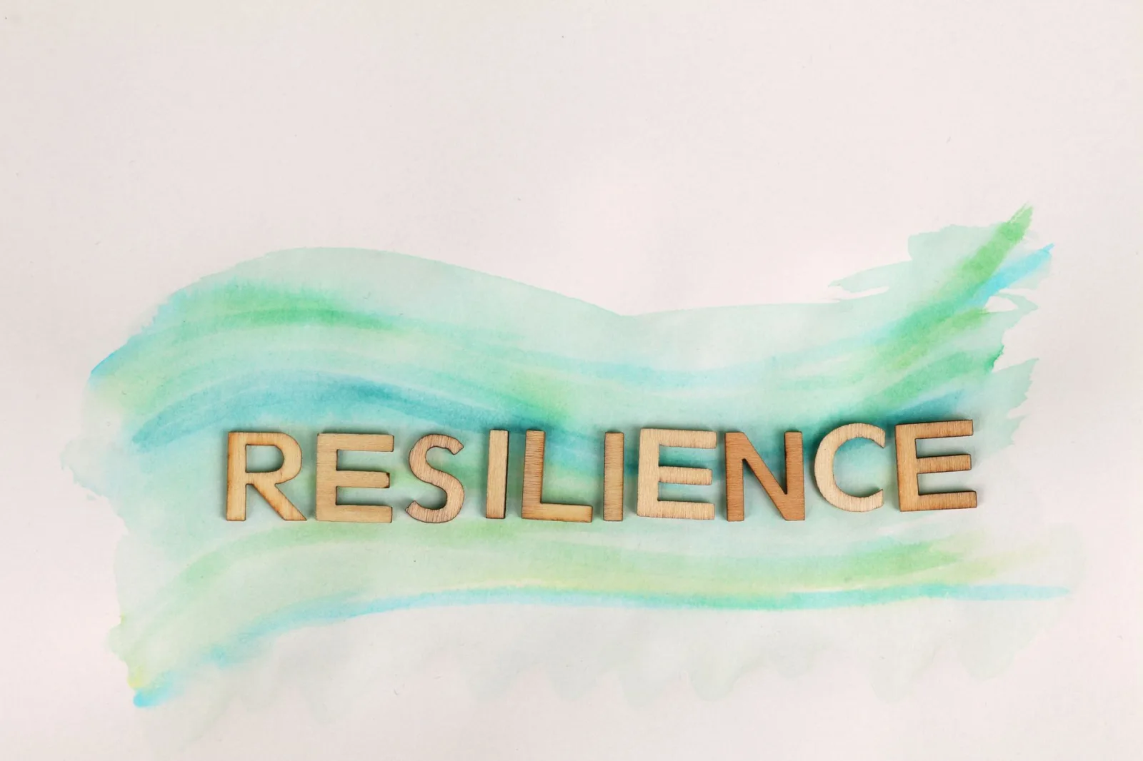 The word 'Resilience' painted with green watercolor and wooden letters on a white background.