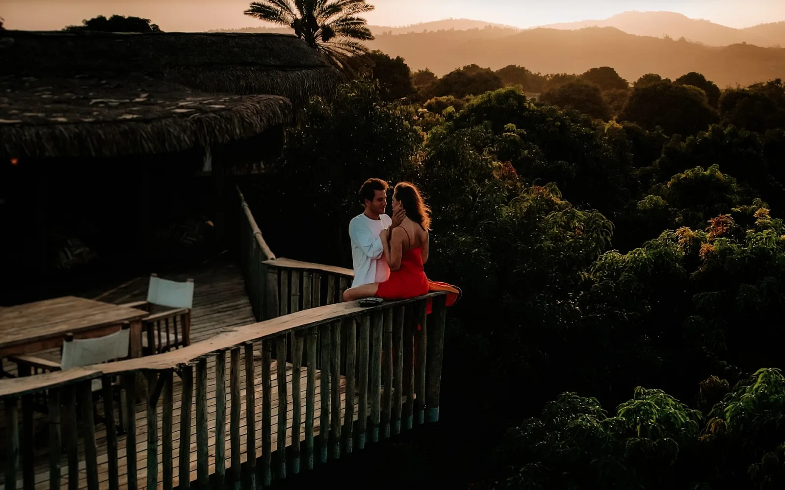 Couple embracing on a wooden viewing deck at sunset, surrounded by lush greenery.