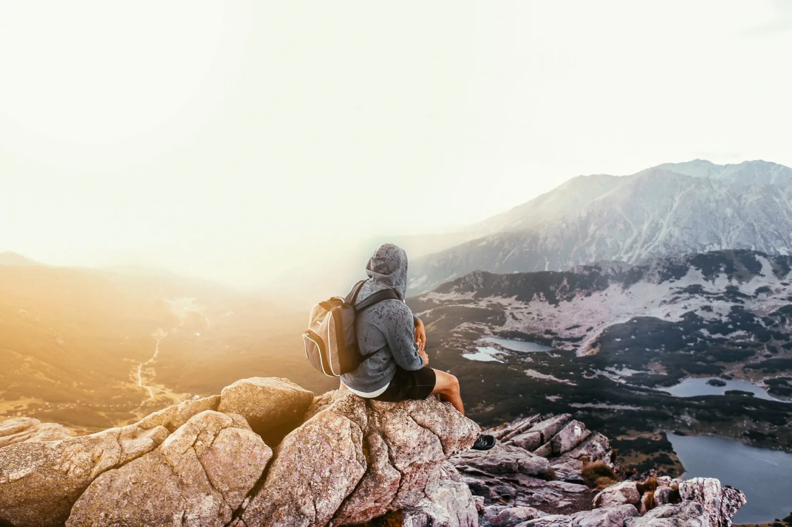 A lone traveler with a backpack sitting on a mountain rock, enjoying the scenic sunrise view.