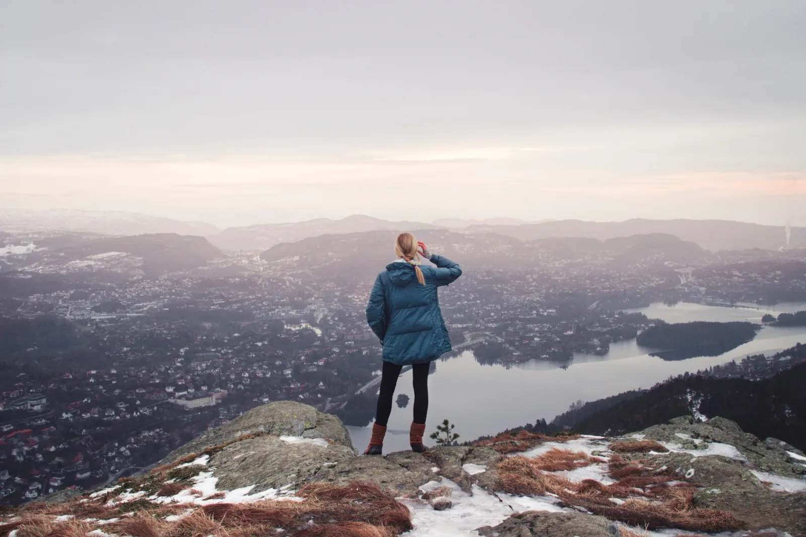 A woman stands on a mountain peak, overlooking a vast, scenic winter landscape.