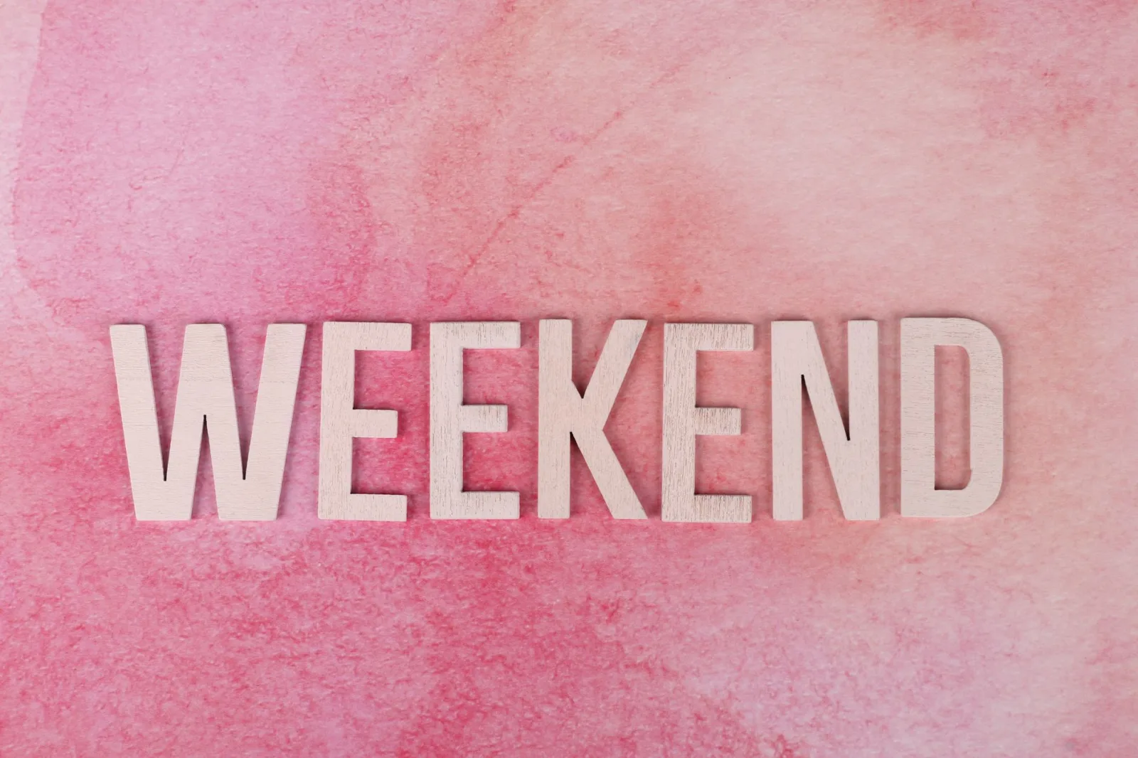 Creative display of the word 'Weekend' in wooden letters on a textured pink background.