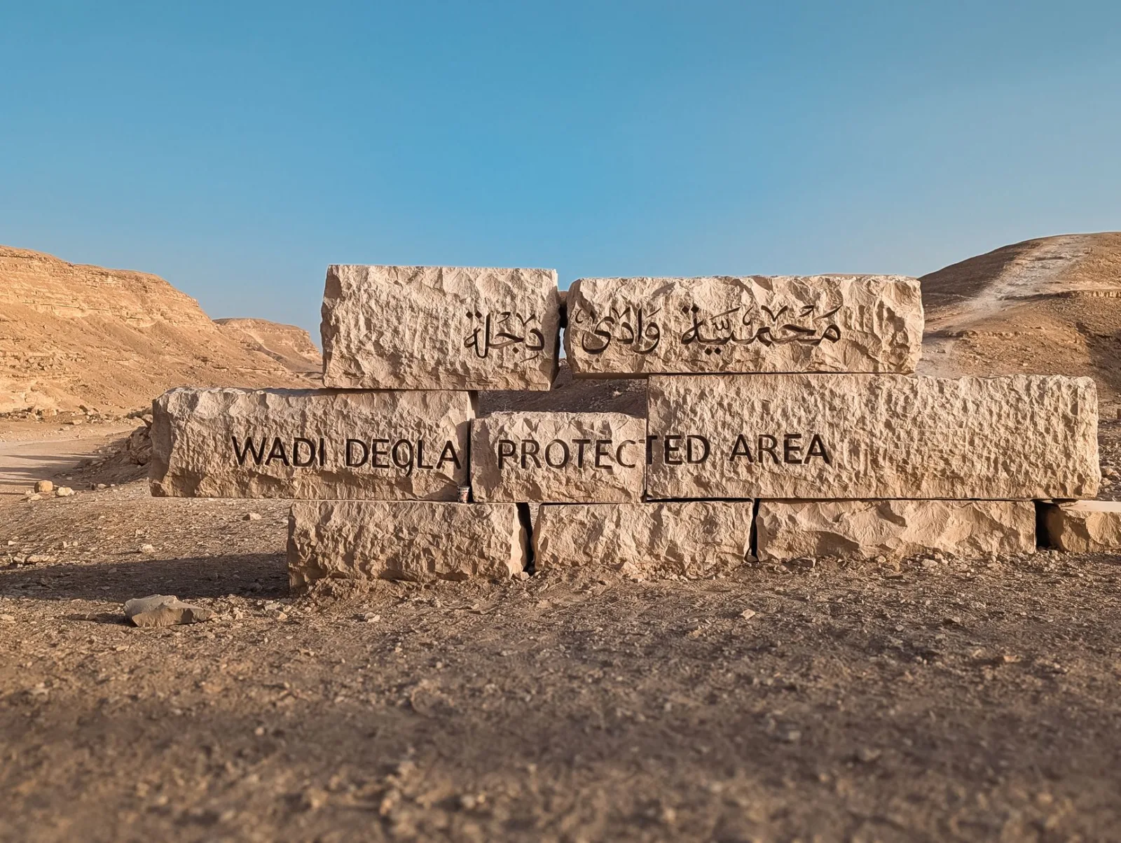 Stone sign marking the entrance to Wadi Degla Protected Area in Egypt's desert landscape.
