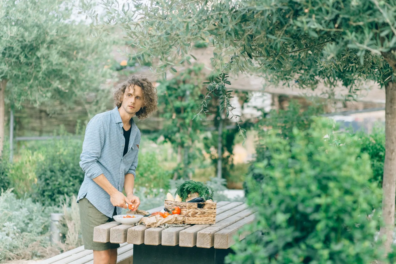 An adult man preparing fresh vegan ingredients at a picnic table in a lush outdoor setting.