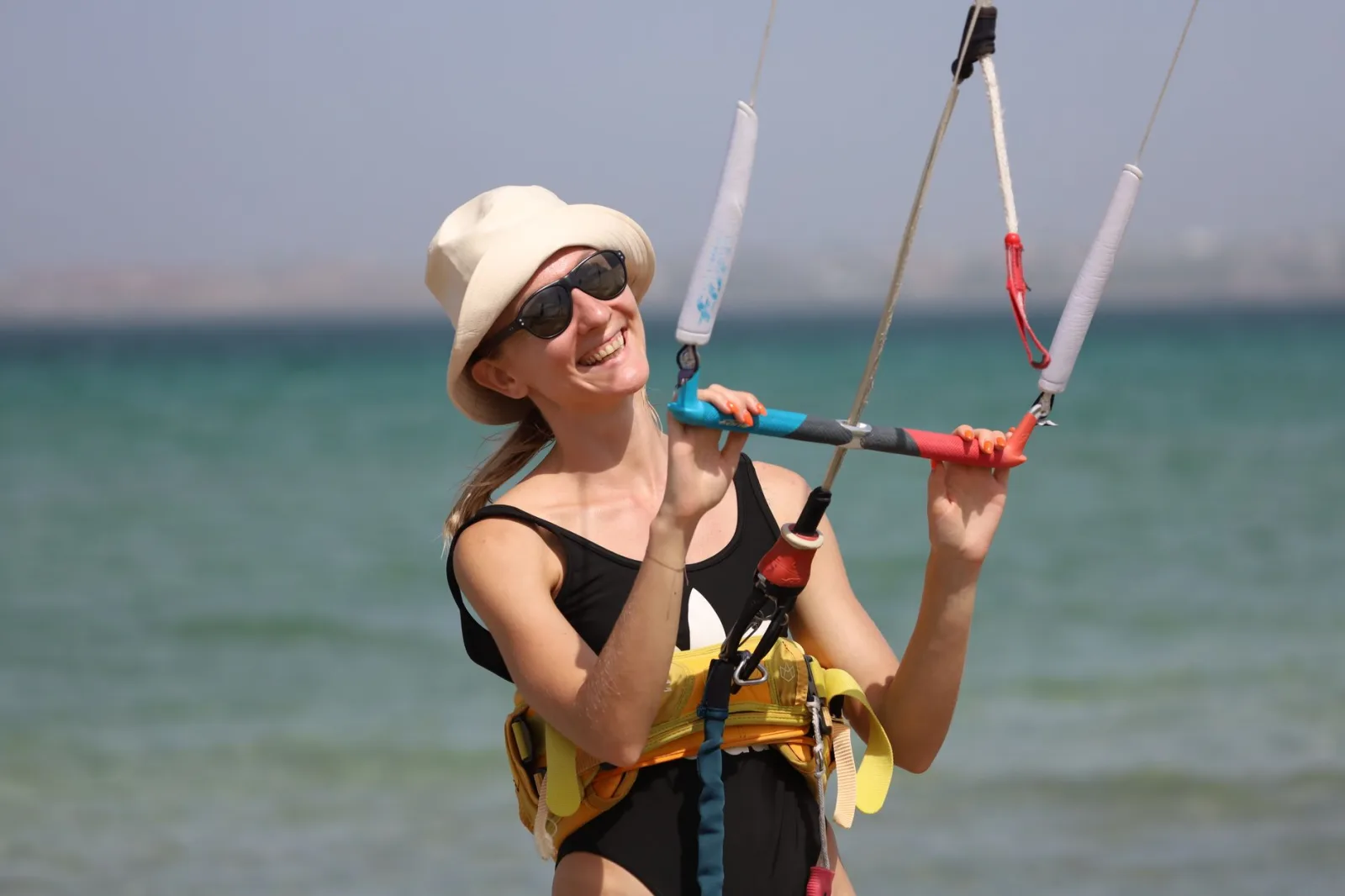 Smiling woman kitesurfing on a sunny day, having fun at the ocean.
