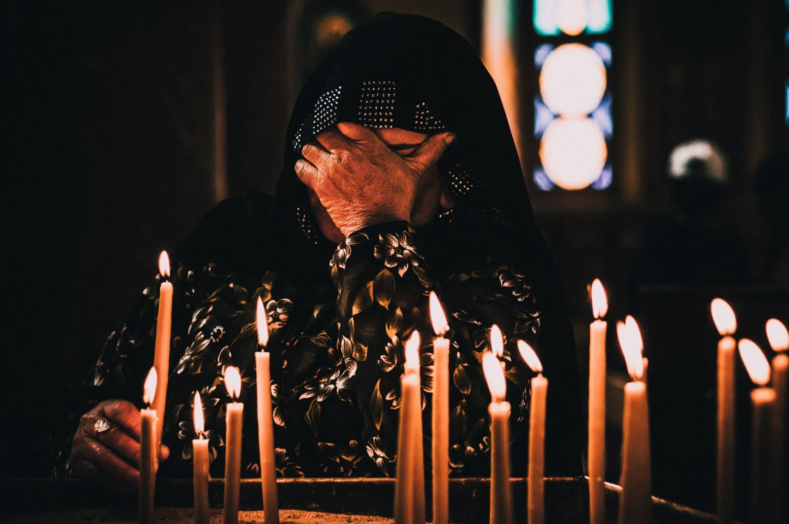 A woman shrouded in a black hijab prays in candlelight inside a Cairo temple.
