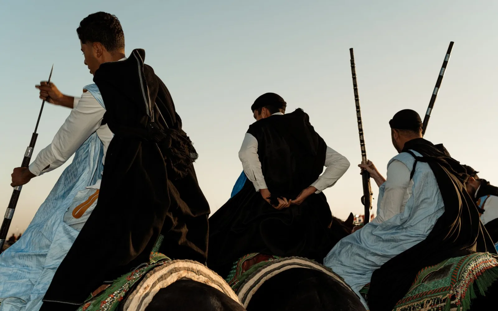 Men in traditional attire participate in a Moroccan equestrian show at sunset.