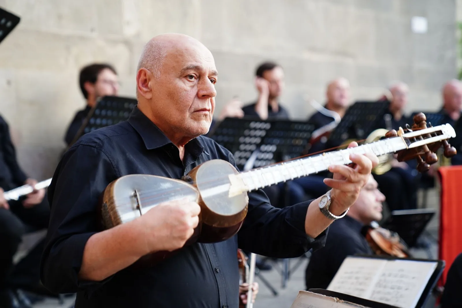 Elderly musician passionately playing a tar in an outdoor concert with an orchestra.