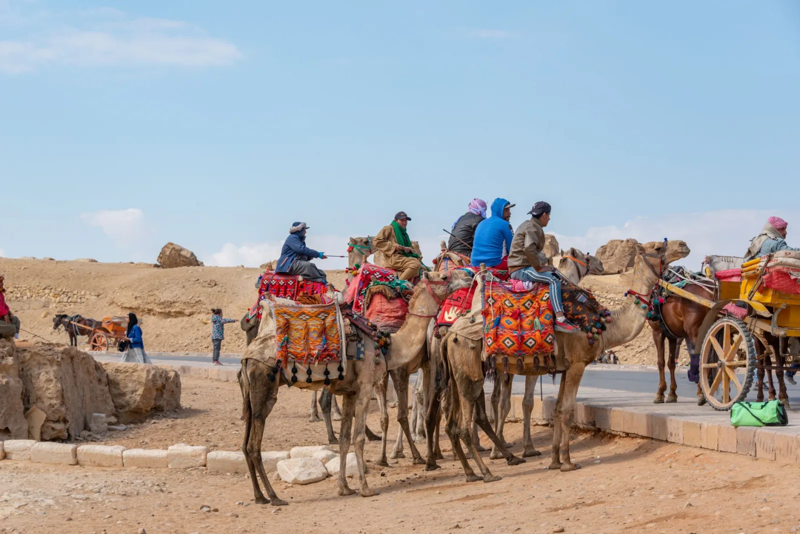 Group of tourists riding camels with colorful saddles in the Egyptian desert, clear sky in the background.