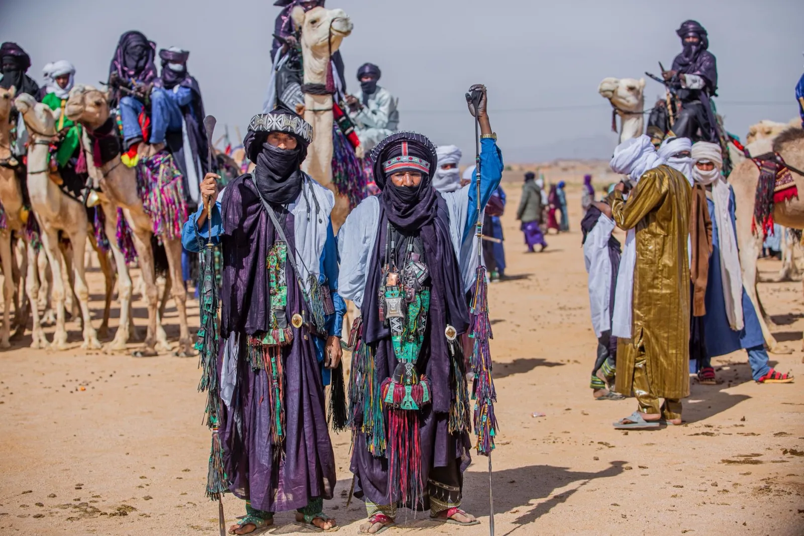 Colorful Tuareg nomads with camels display traditional attire at a desert festival.