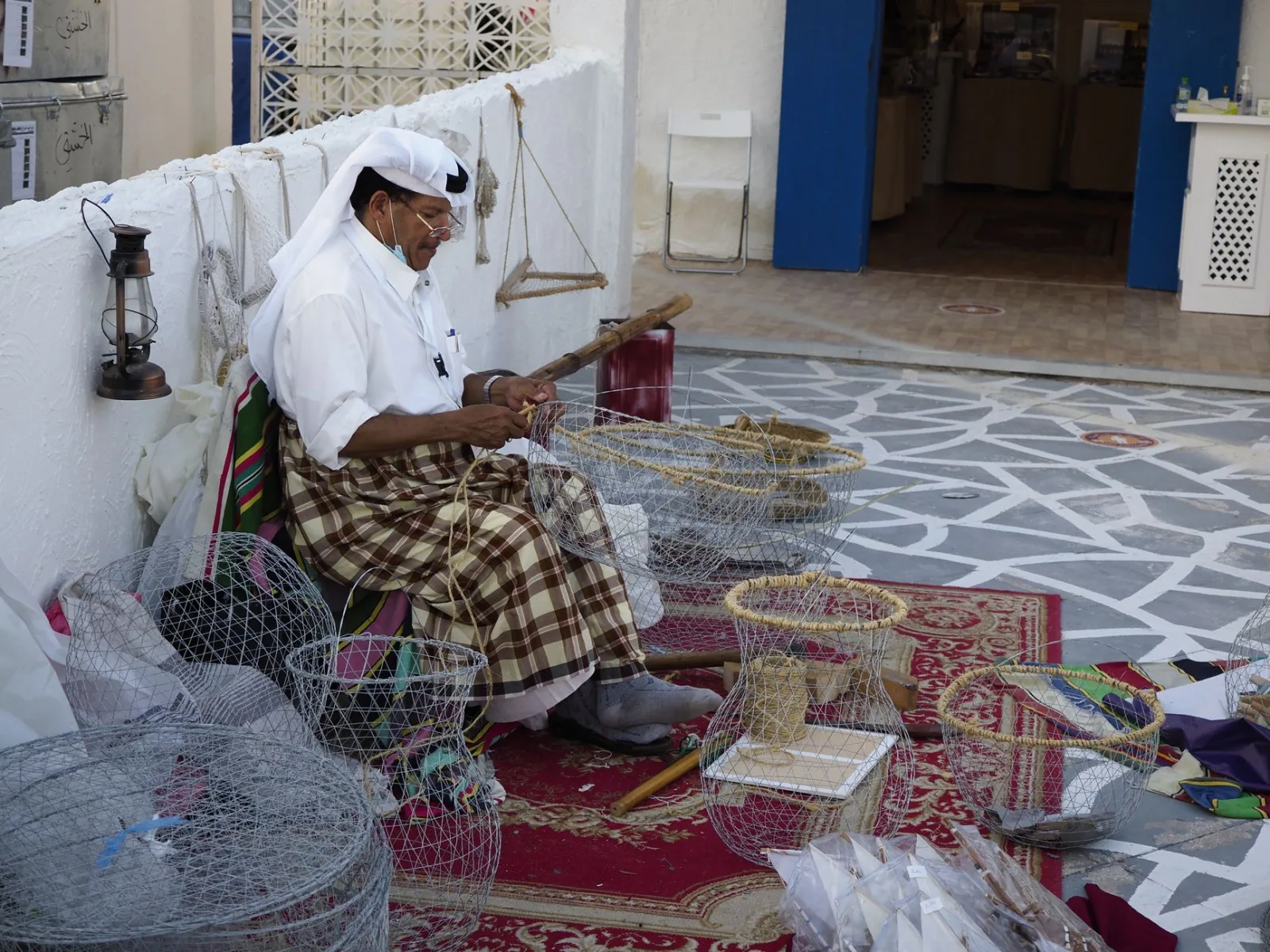 Elderly man creating wire baskets in a traditional market setting.