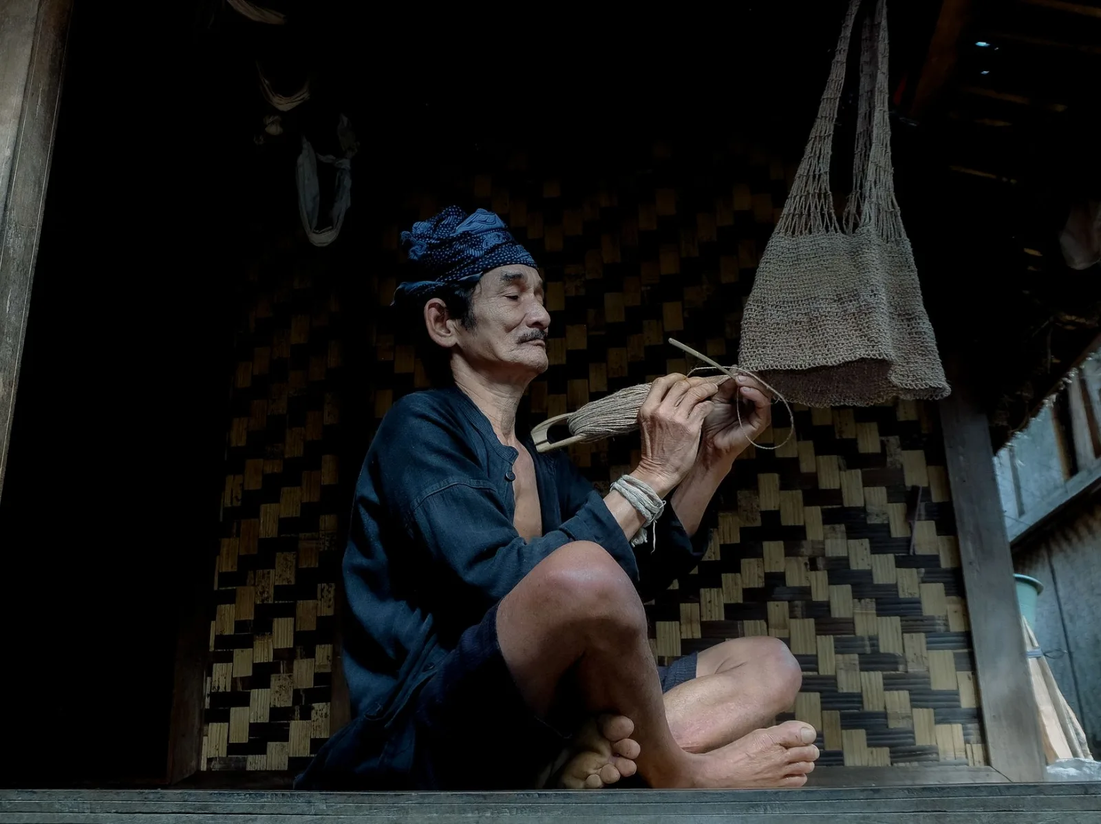 Elderly man crafting a traditional basket in a rustic setting, showcasing handmade skills.