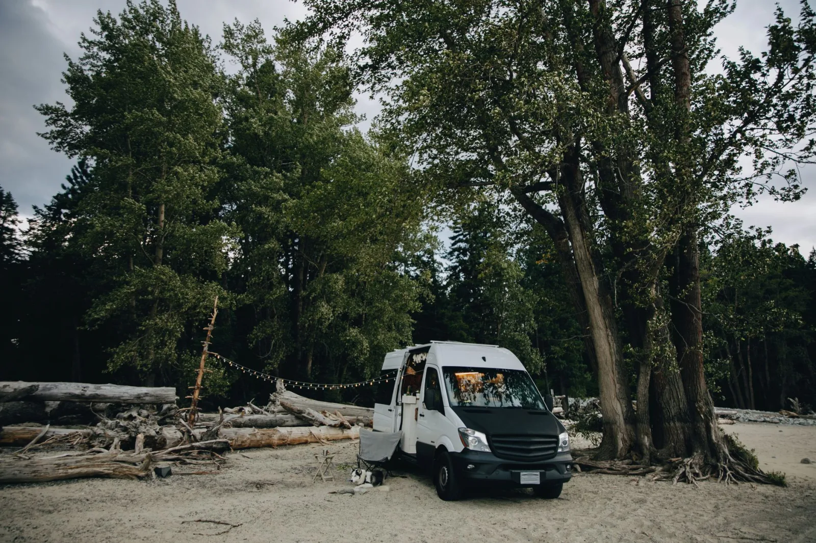A cozy camper van parked by the forest edge on a serene sandy beach, perfect for adventurous travelers.