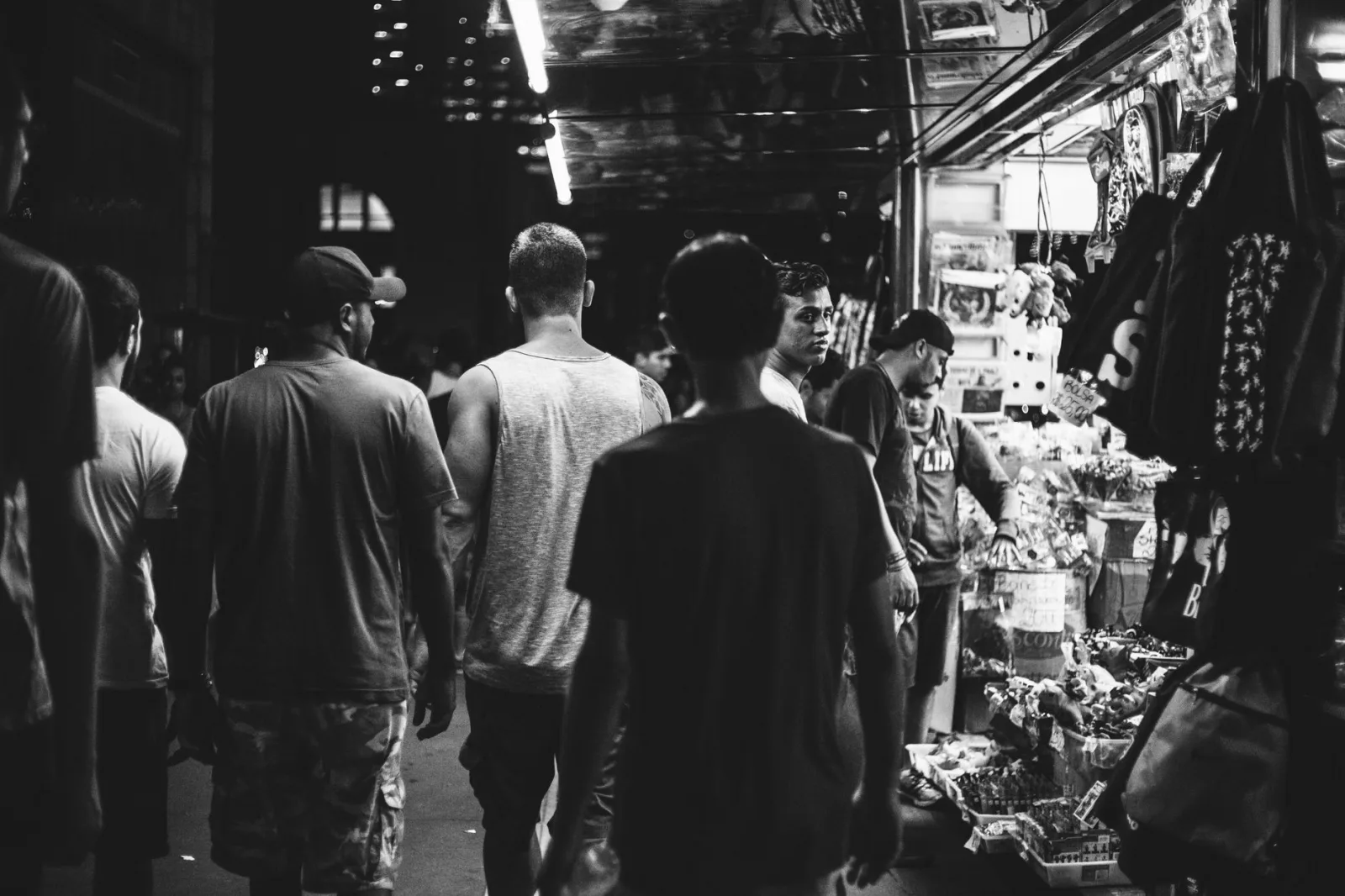 A bustling night market scene captured in black and white, showcasing shoppers and vibrant stalls.