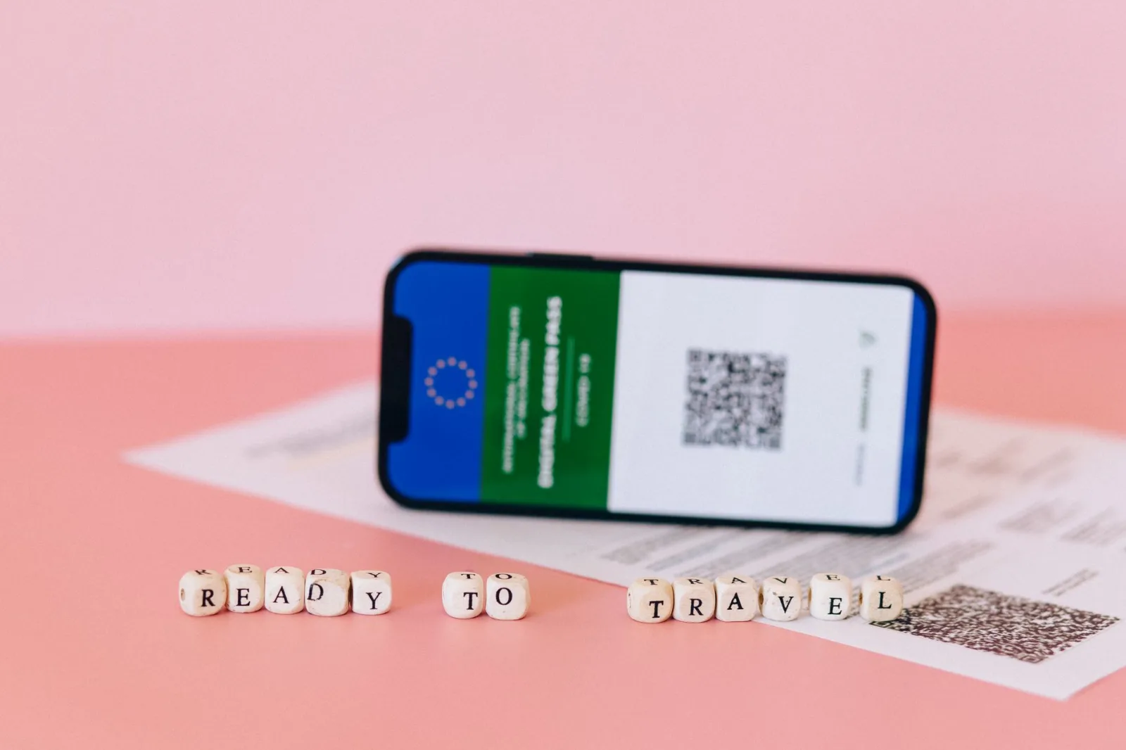 Smartphone displaying digital green pass on a pink surface with travel beads.