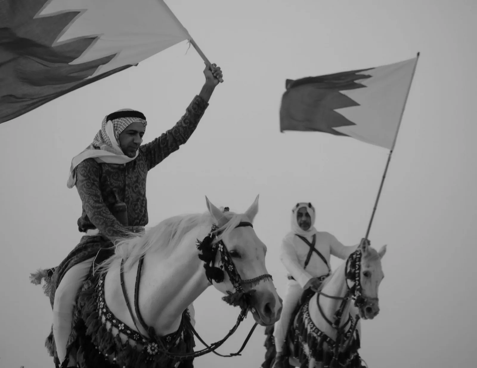 Bahraini horsemen ride with national flags, showcasing patriotism and tradition.