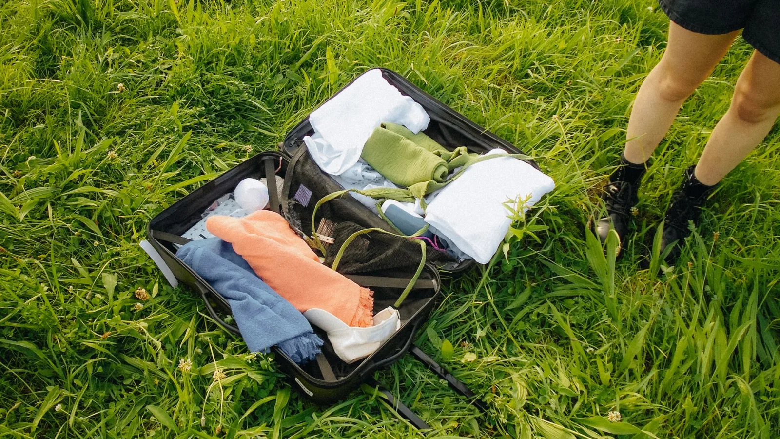 A packed suitcase open on grass, showcasing travel essentials in a sunny outdoor setting.