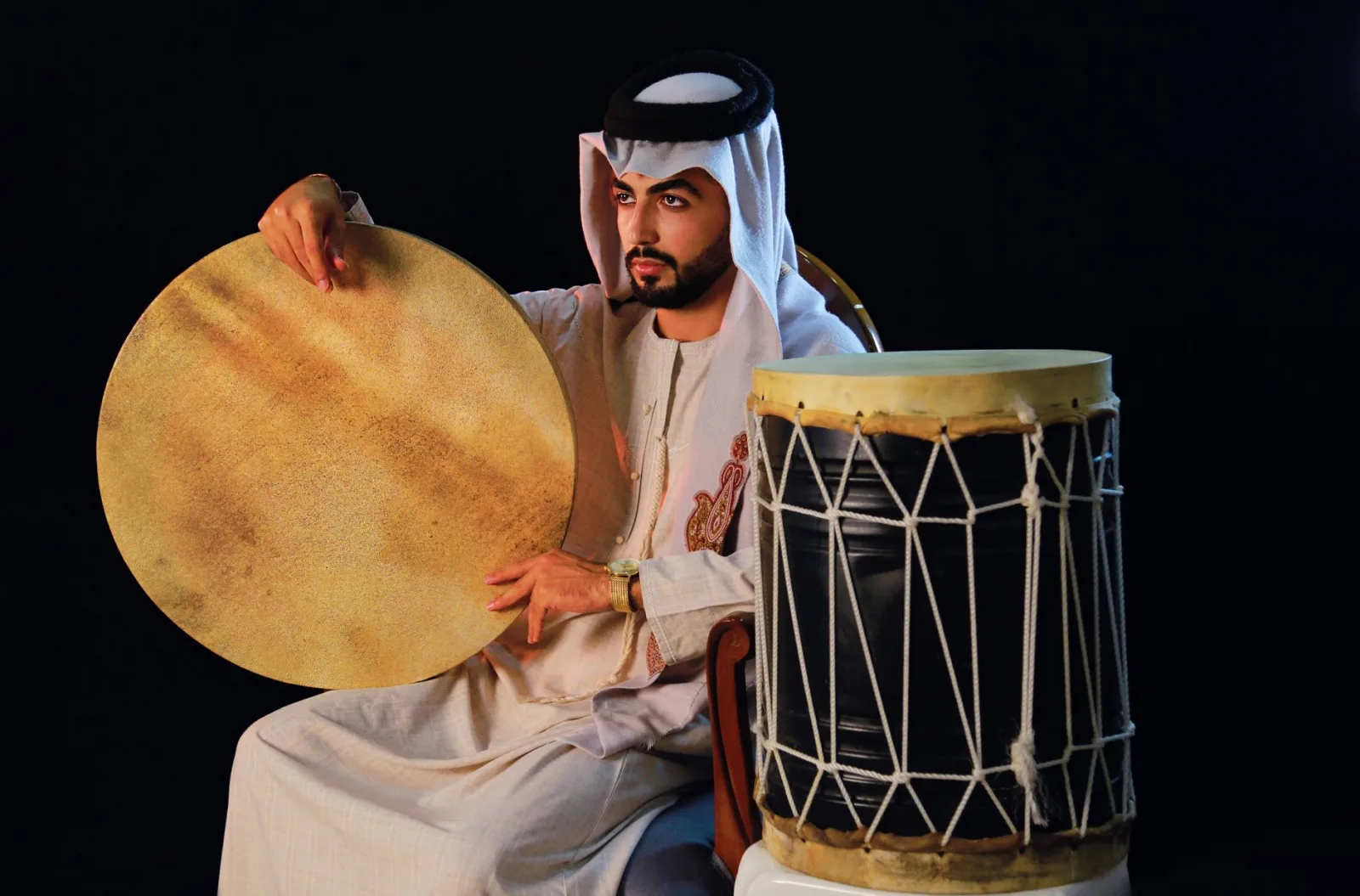 Middle Eastern man in traditional attire holding an Arabic drum, showcasing cultural heritage.