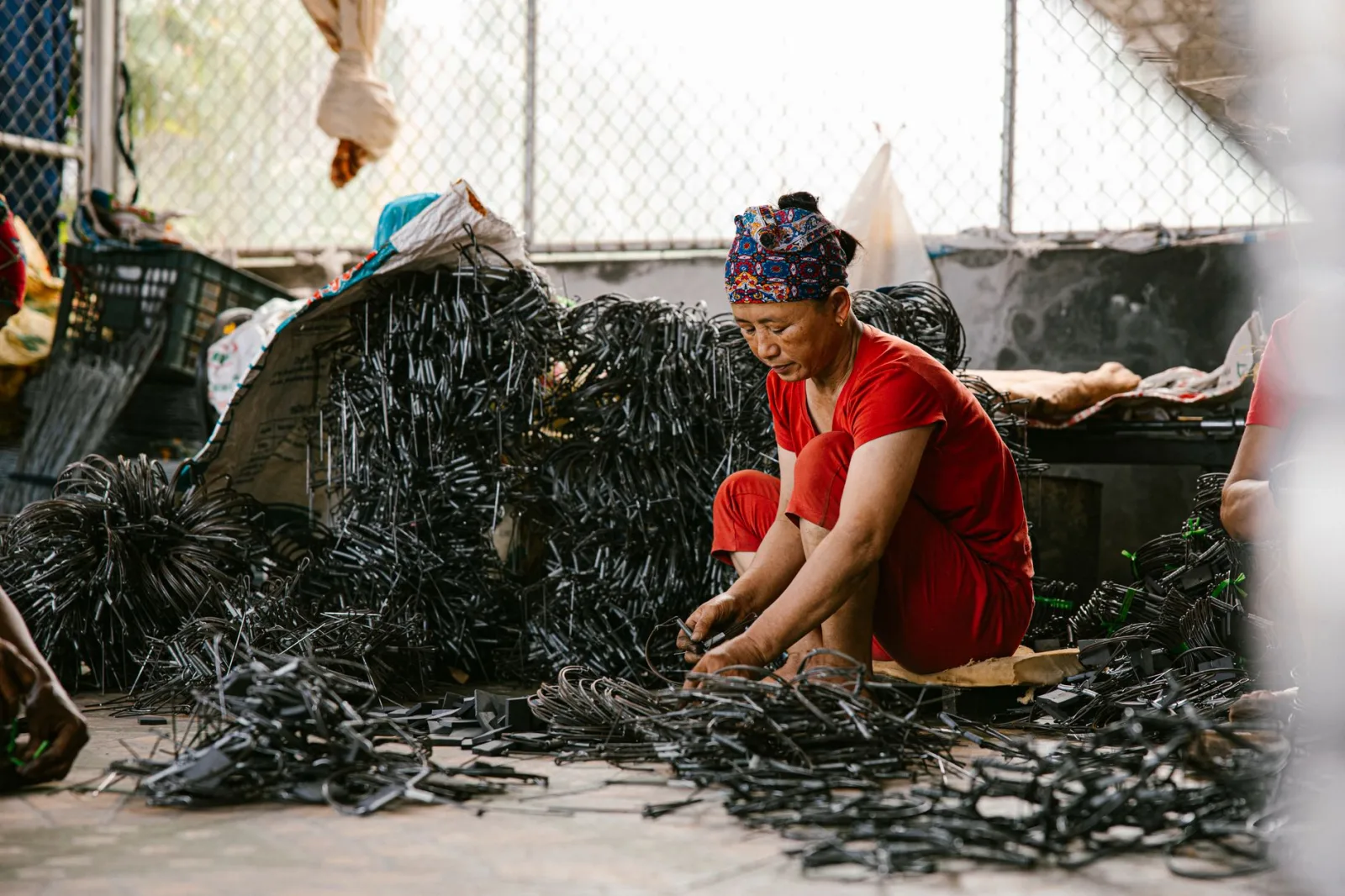 A woman in a red outfit sorts recycling materials in an indoor warehouse setting, highlighting sustainability practices.