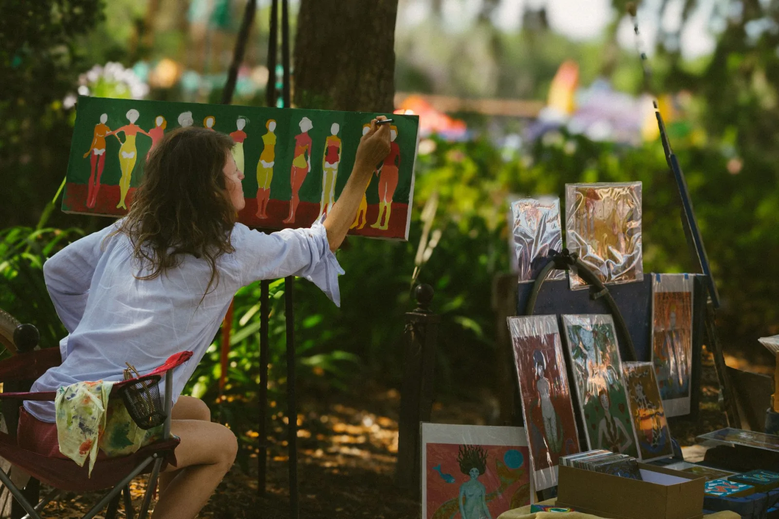 Artist painting colorful artwork outdoors in a park setting in Greenville, SC, during a sunny day.