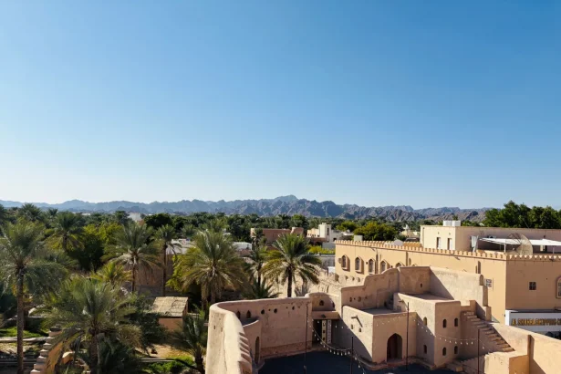 View of Nizwa Fort and the surrounding oasis against Hajar Mountains under a clear blue sky.