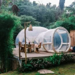 Cozy transparent bubble tent located on wooden platform near dining table in tropical forest