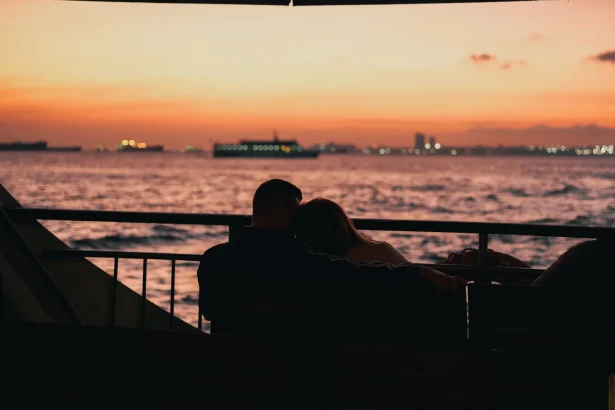 A couple embraces while watching the sunset over the sea, creating a romantic silhouette.