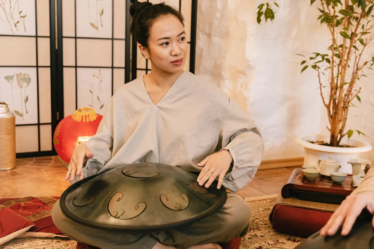 An Asian woman playing a steel tongue drum in a cozy indoor setting. Peaceful and cultural ambiance.