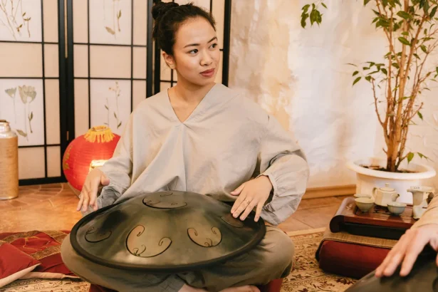 An Asian woman playing a steel tongue drum in a cozy indoor setting. Peaceful and cultural ambiance.