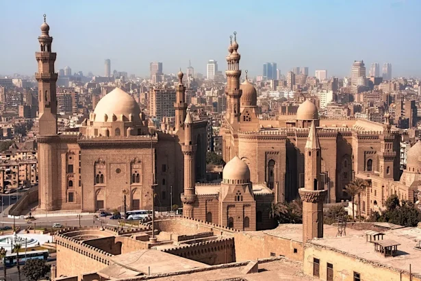 Aerial view of historic mosques with Cairo cityscape backdrop, showcasing Islamic architecture.