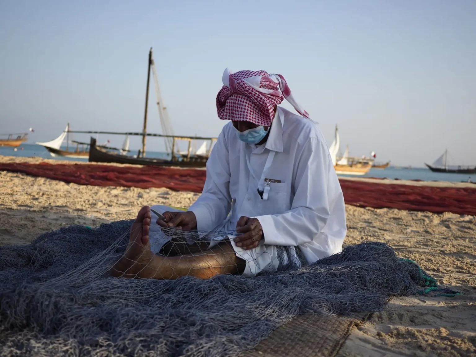 A traditional fisherman repairs nets on a beach in Doha, Qatar.