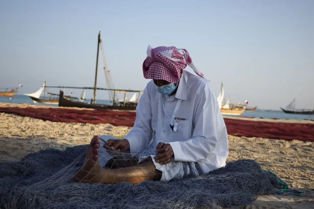 A traditional fisherman repairs nets on a beach in Doha, Qatar.