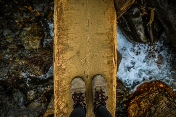 View of a person standing on a narrow wooden bridge over rushing river rapids.