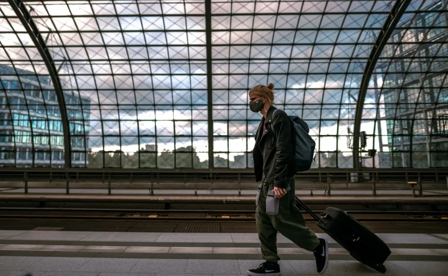 A person with a mask in a railway station, pulling luggage and embracing urban travel life.