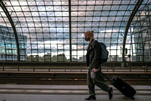 A person with a mask in a railway station, pulling luggage and embracing urban travel life.