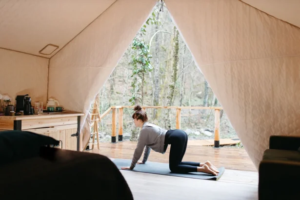A woman performs yoga inside a tent with a tranquil outdoor view, promoting wellness and relaxation.