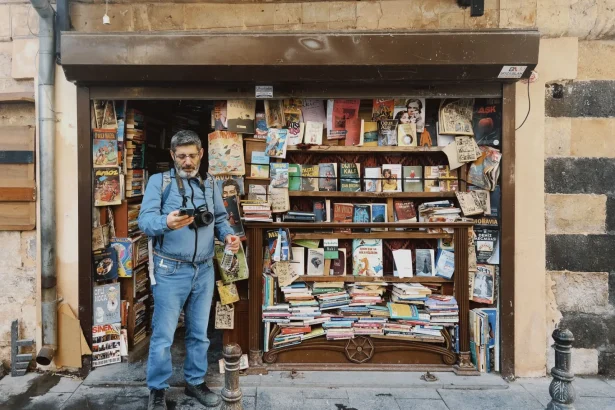 A quaint street bookstore stocked with diverse titles and a photographer capturing the moment.