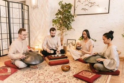 A diverse group meditates with handpans and tea in a serene, indoor setting.