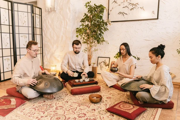 A diverse group meditates with handpans and tea in a serene, indoor setting.