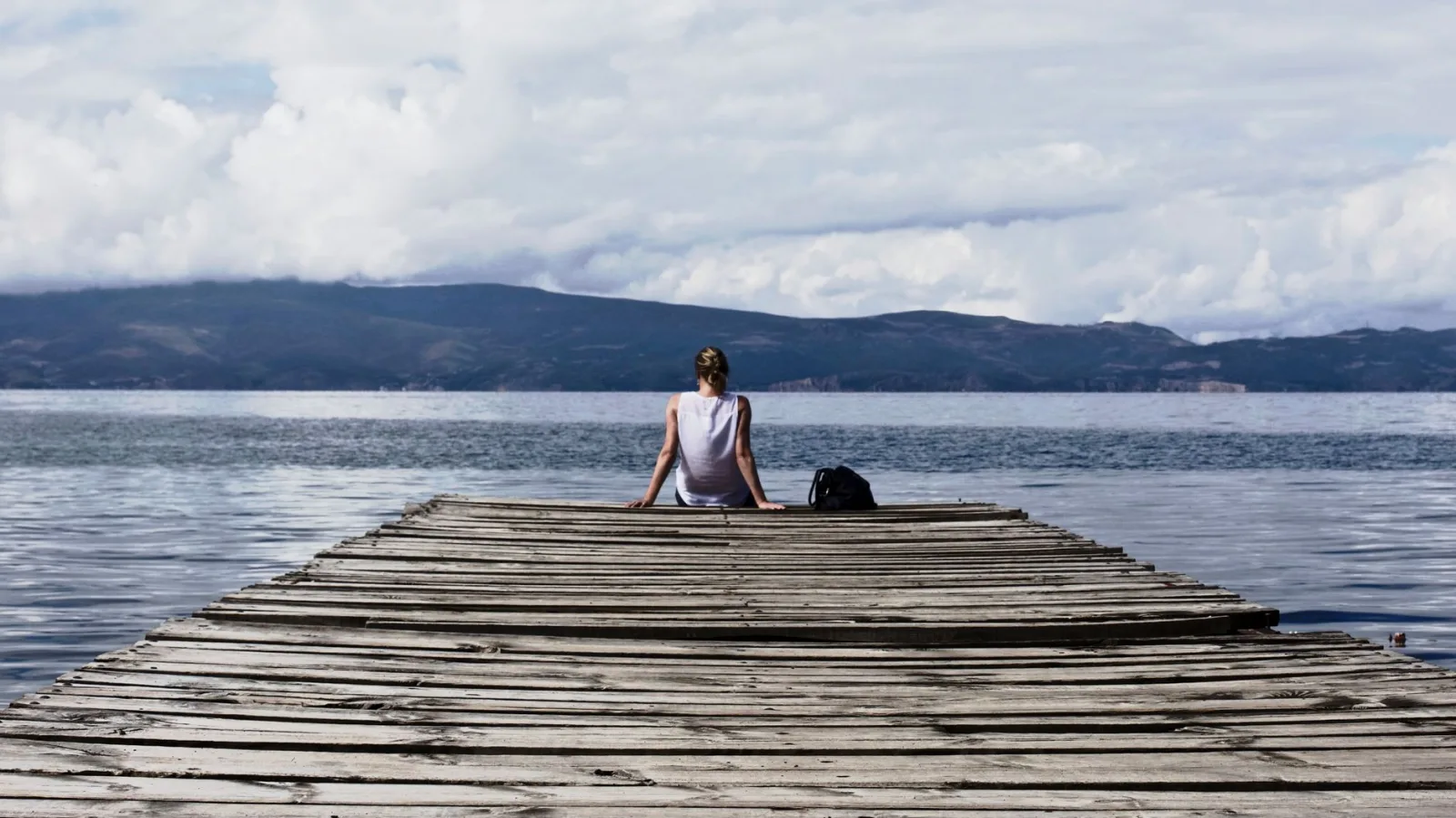 Woman sitting on a wooden pier, enjoying the serene lake view and mountains.