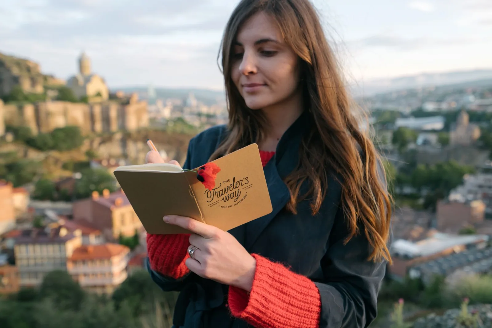 A woman writes in her journal against a backdrop of a historic cityscape.