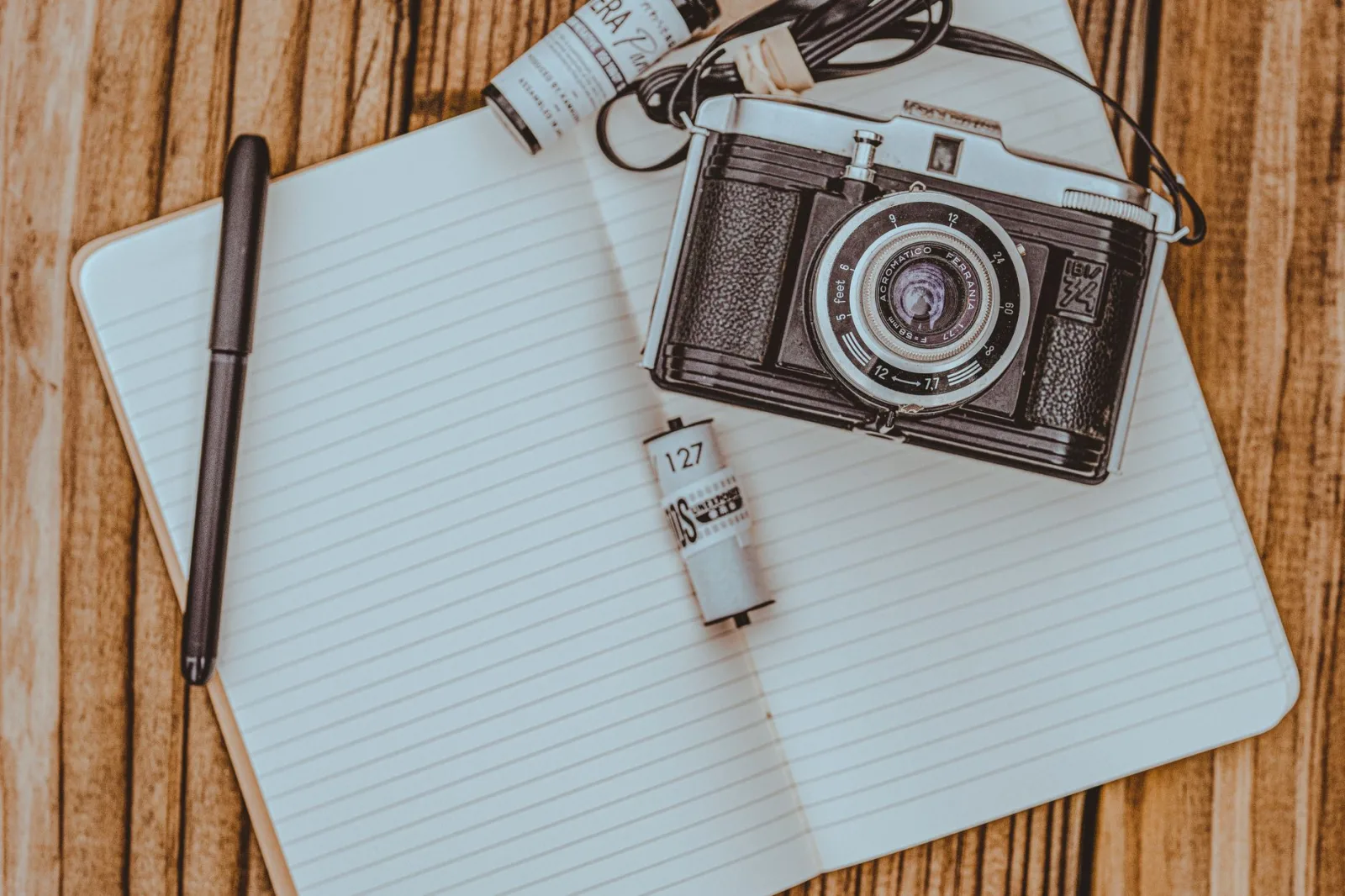 Flat lay of a retro camera on a wooden table with a notepad and film roll.