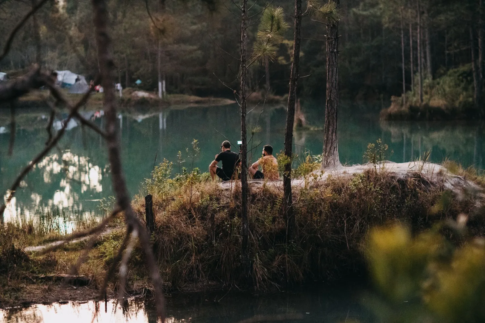 Two friends enjoy a peaceful camping experience by a forested lake.